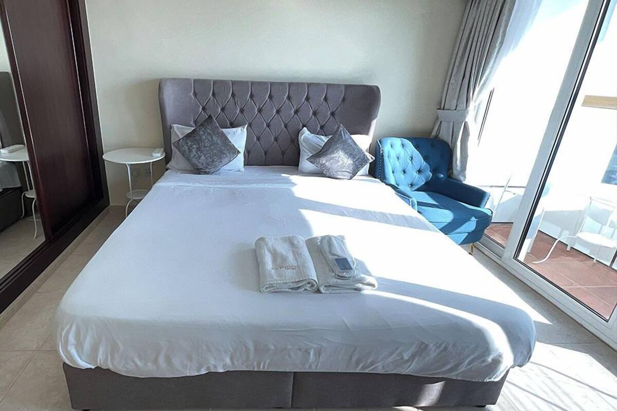 A large bed with a tufted headboard, multiple pillows, and a neatly folded towel.