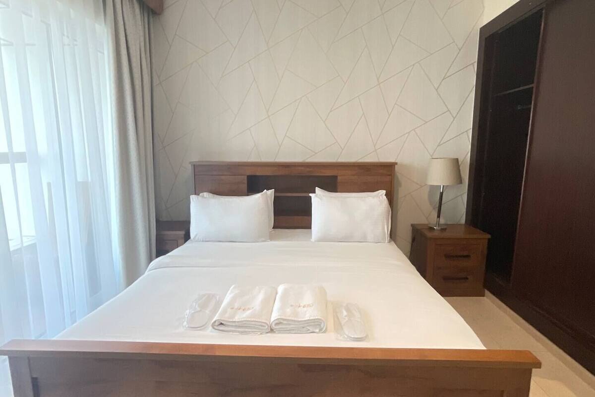 A hotel room with a large bed, a wooden headboard, a nightstand with a lamp, and a wardrobe.