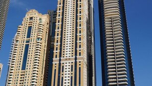 A tall, modern skyscraper with a unique architectural design, featuring multiple balconies and a prominent entrance at the base. - Marina Marvel Room Elite Residences (Dubai)