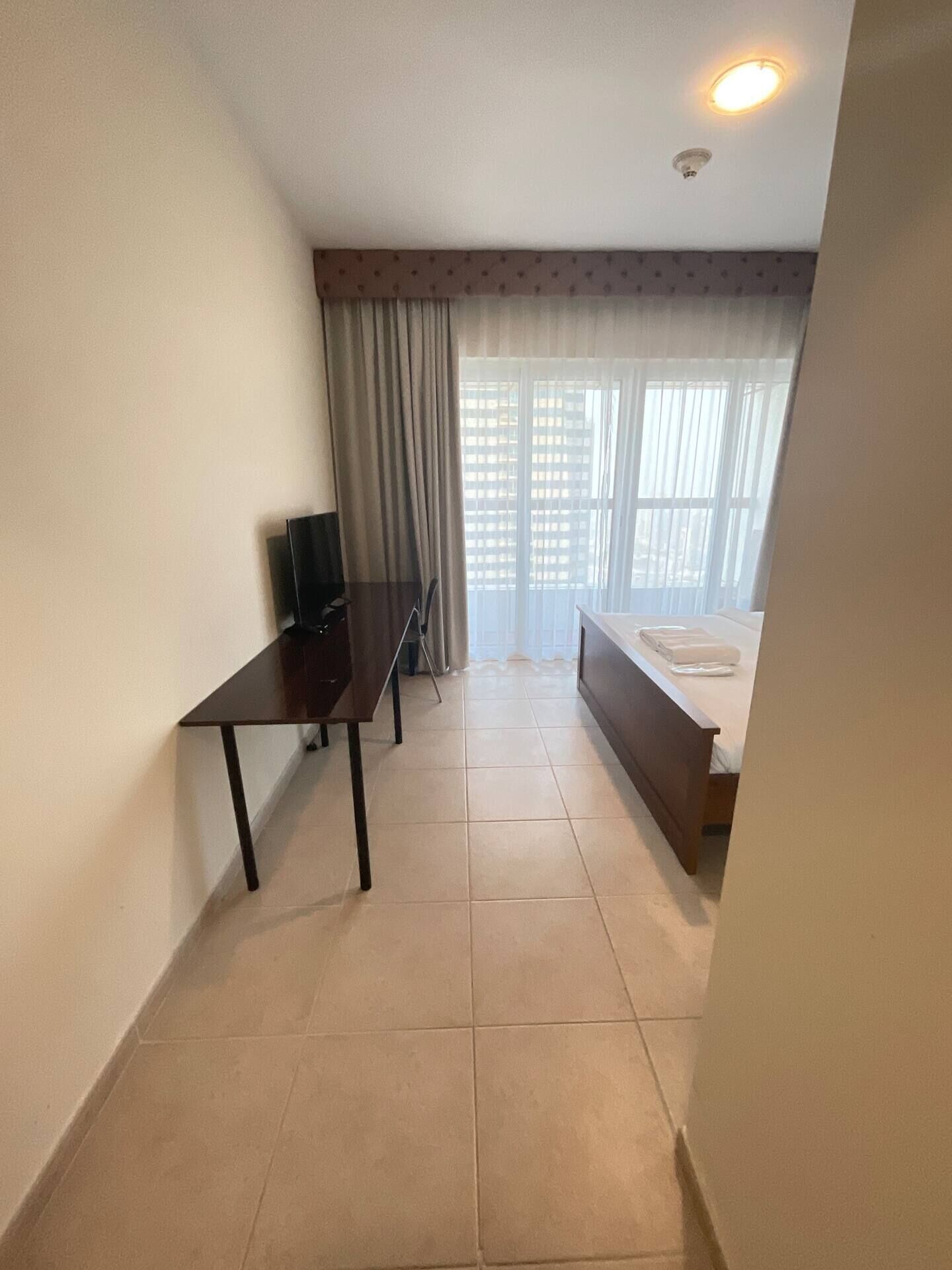 Una habitación pequeña y limpia con una cama, un escritorio y un televisor.