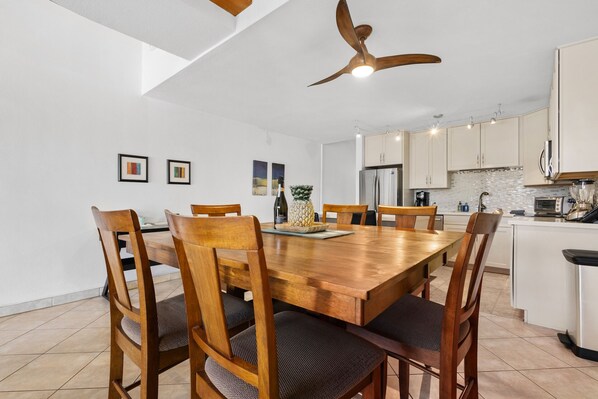 A modern kitchen with white cabinets, a wooden dining table, and a ceiling fan. - Luxury Aloha Spirit Oceanview Penthouse Sleeps 5 (Kihei)