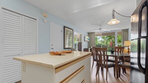 A kitchen with a wooden countertop, white cabinets, a dining area with a table and chairs, and a view of greenery outside.