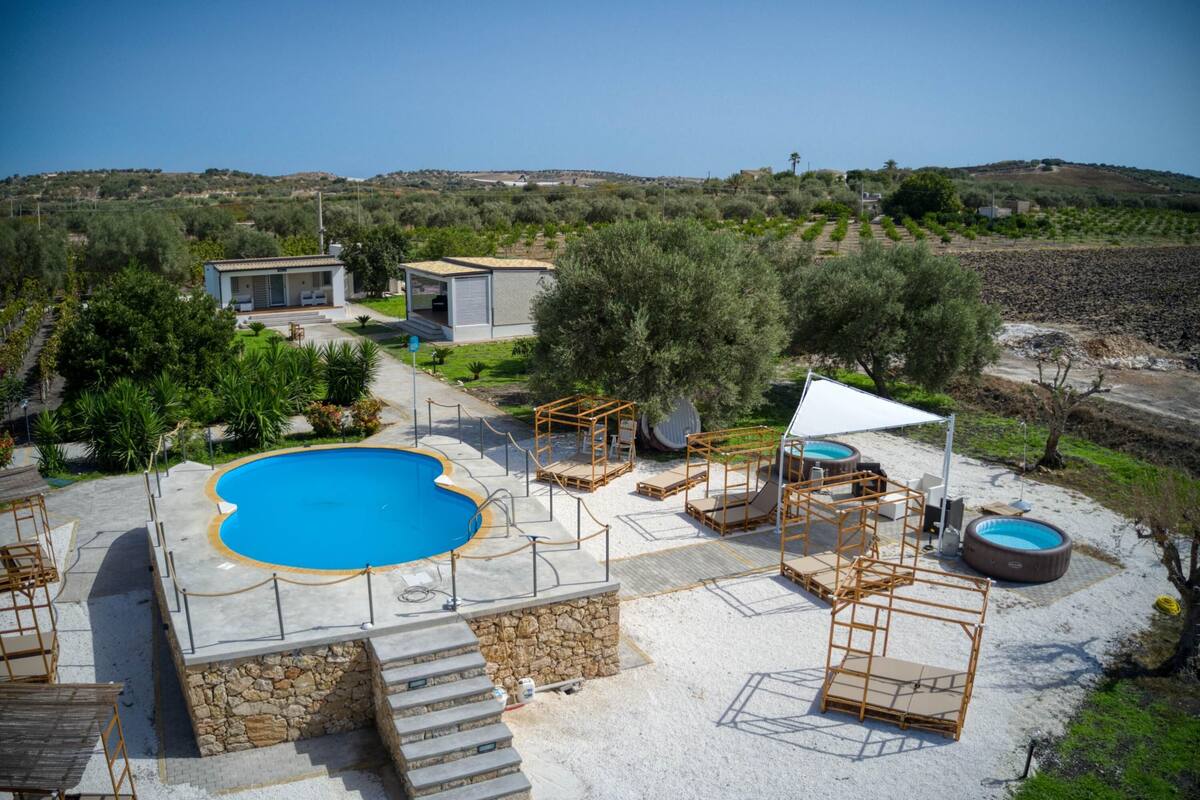 A pool area with a large pool, sun loungers, and a small building.