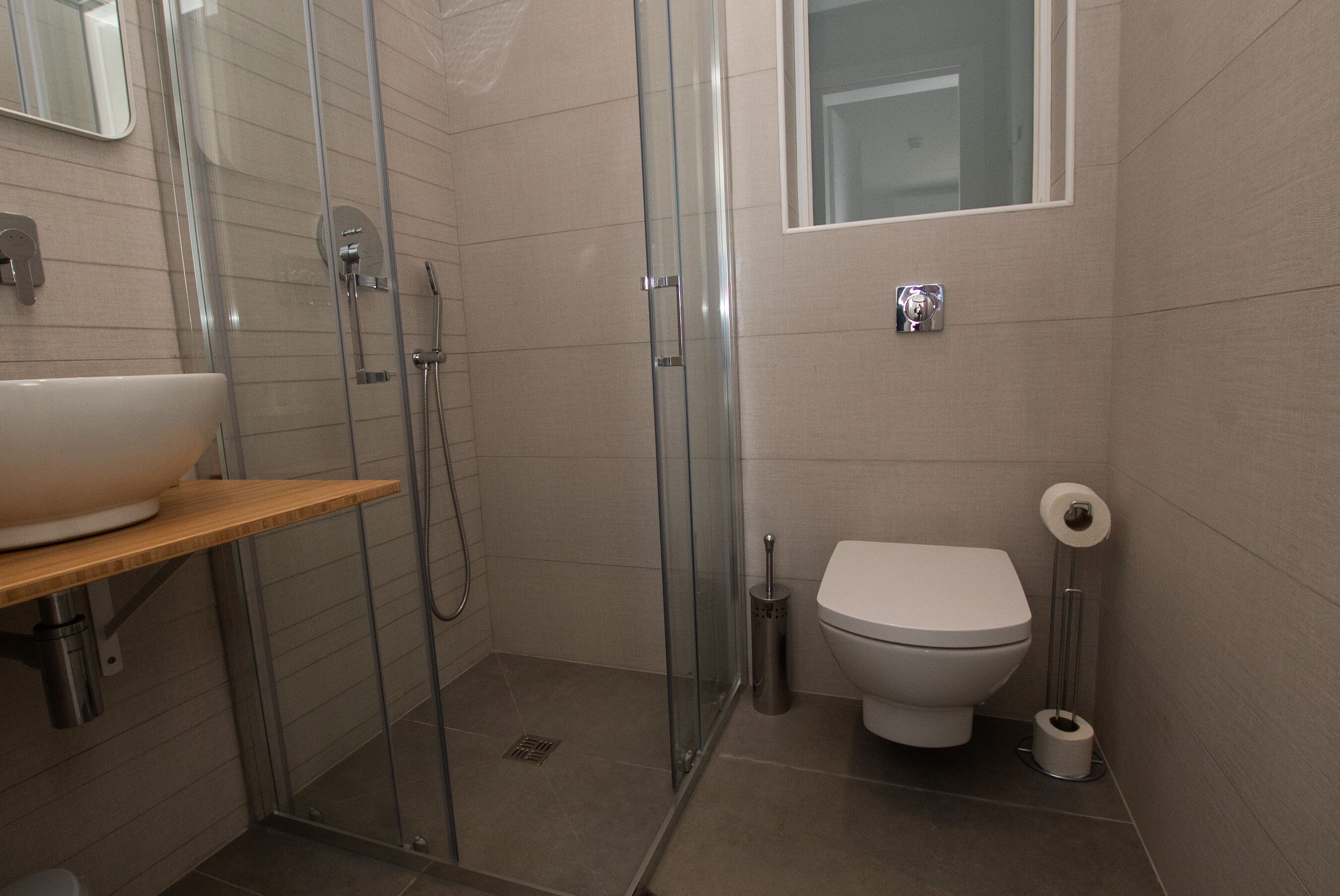 Ein modernes Badezimmer mit einer in Glas abgeschirmten Dusche, einer Toilette und einem Waschbecken auf einem Holzregal.