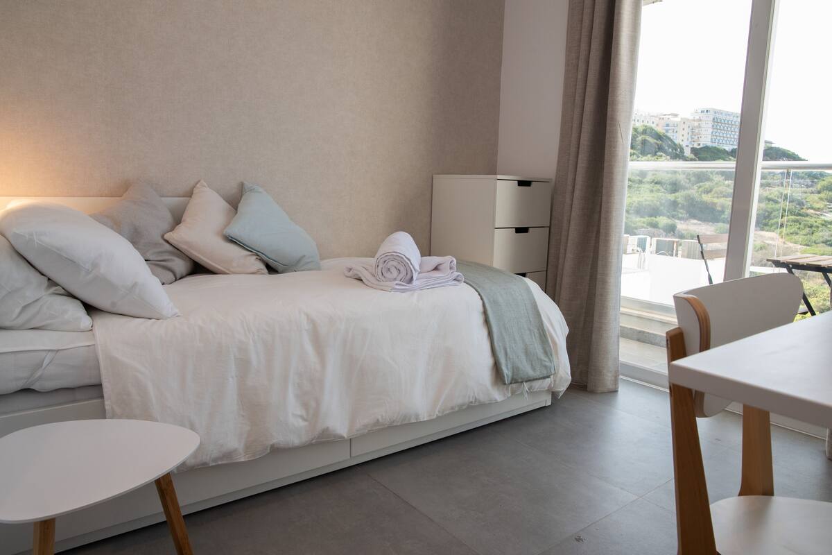 Ein modernes Hotelzimmer mit Bett, Nachttisch, Lampe und Blick auf die Stadt.