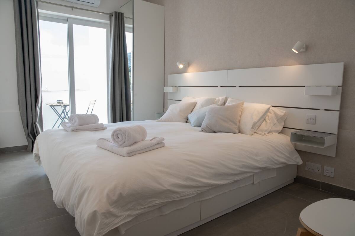 Ein modernes Hotelzimmer mit einem großen Bett, einem Nachttisch und Blick durch ein großes Fenster.