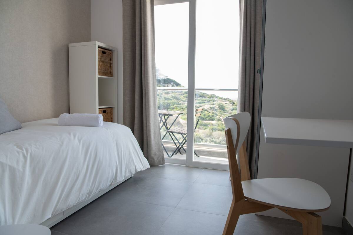 Ein Schlafzimmer mit einem Bett, einem Holzstuhl, einem Schreibtisch und einem weißen Kleiderschrank.