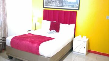 A hotel room with a bed, a ceiling fan, a framed picture on the wall, and a small white cabinet.
