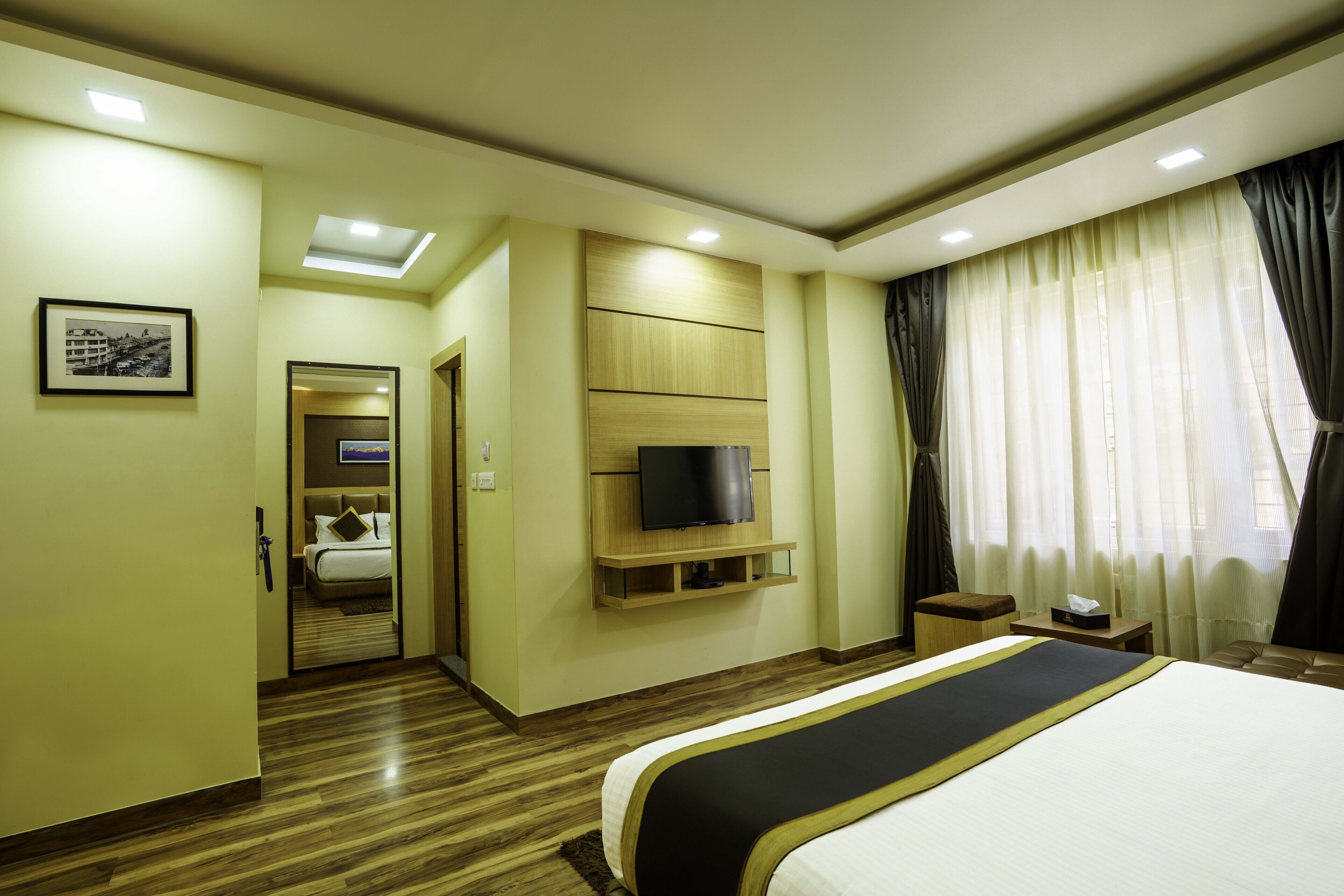 Una camera d'albergo con un letto grande, una televisione a parete, un pavimento in legno e una finestra con tende.