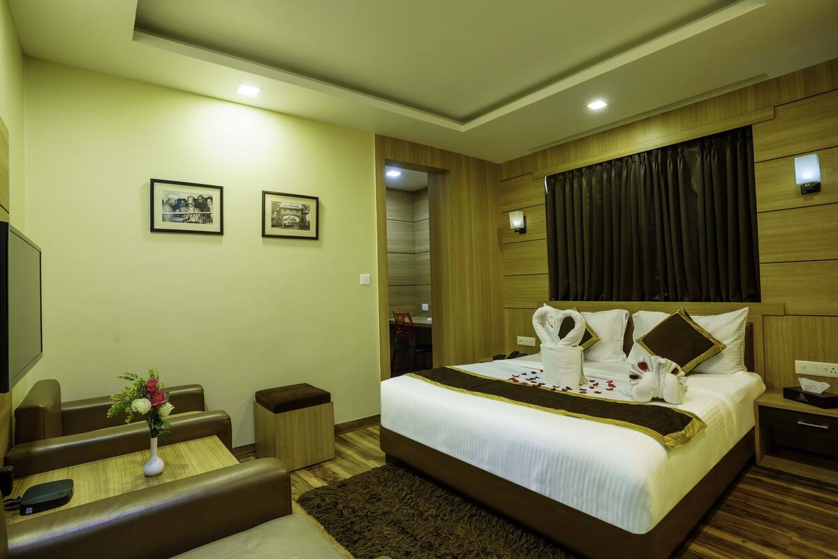 A hotel room with a large bed, a desk, a chair, and a small table with a vase of flowers.