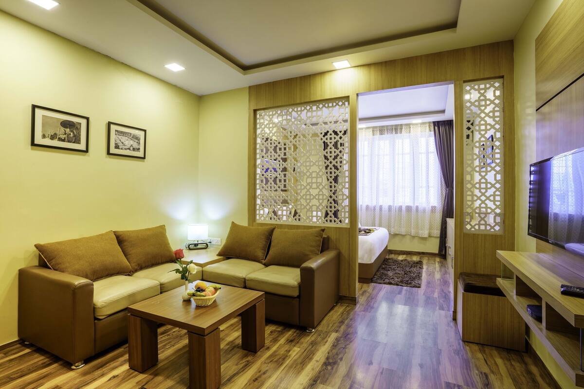 A modern living room with a sofa, coffee table, and TV. There are two framed pictures on the wall and a decorative screen.