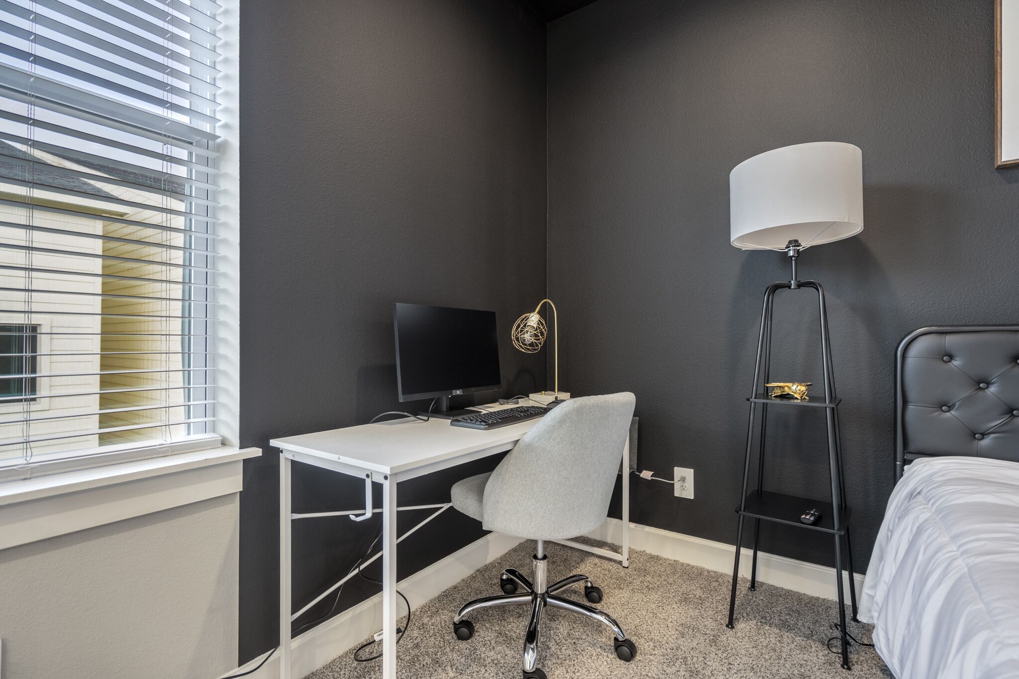 A bedroom with a desk, a chair, a bed, a lamp, and a window with blinds.