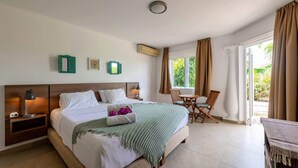 Un dormitorio con cama, mesitas de noche, una pequeña mesa con sillas y un ventanal con cortinas.