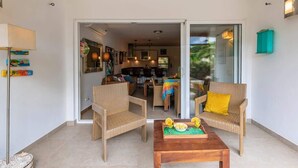 Una sala de estar moderna con muebles de mimbre, una mesa de centro con fruta y vistas al jardín a través de puertas de cristal.