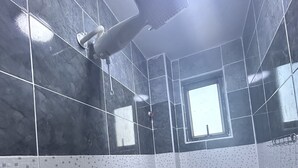 A bathroom with dark tiles, a toilet, a shower, and a window.