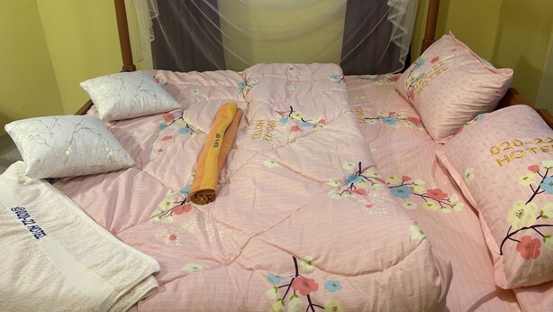 A bed with a floral bedspread, pillows, and a rolled-up towel.