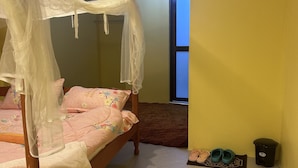 A bedroom with a four-poster bed, a small rug, a trash bin, and a pair of slippers.