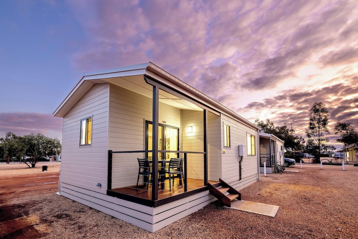 A single-story, white wooden cabin with a covered porch and a small outdoor seating area.