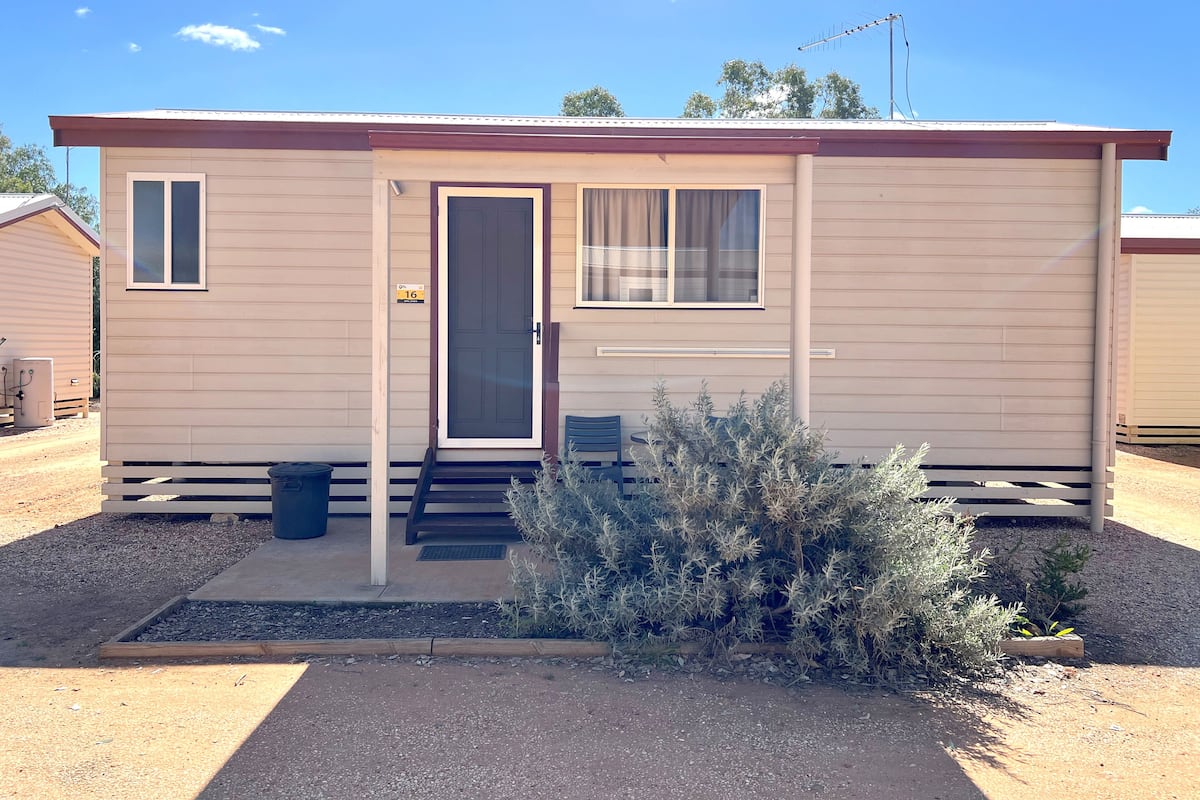 A single-story mobile home with a front door, a small window, and a window with curtains.