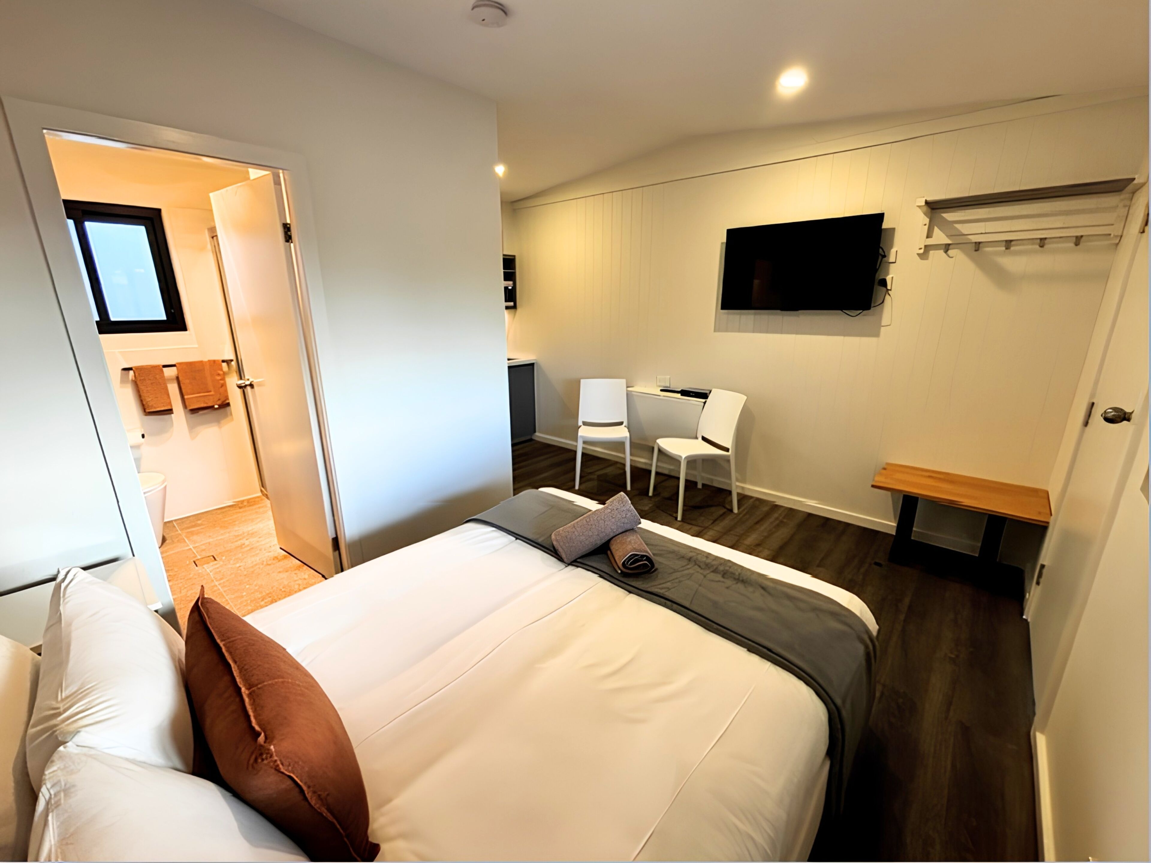 A hotel room with a bed, two chairs, a TV, and a small desk.