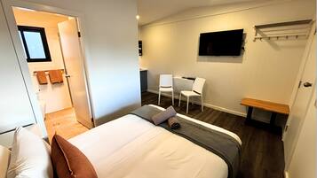A hotel room with a bed, two chairs, a TV, and a small desk.