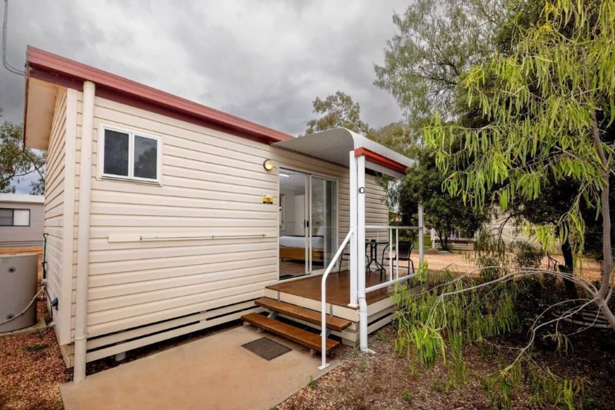 A small, single-story mobile home with a red roof, a front porch, and a small deck.