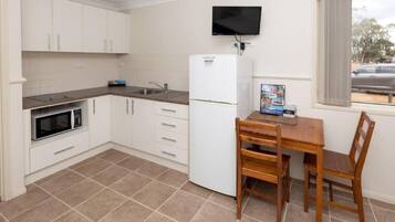 A compact kitchen with white cabinets, a microwave, a refrigerator, and a wooden dining table with chairs.