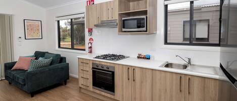 A modern kitchen with wooden cabinets, a gas stove, an oven, a microwave, and a sink.