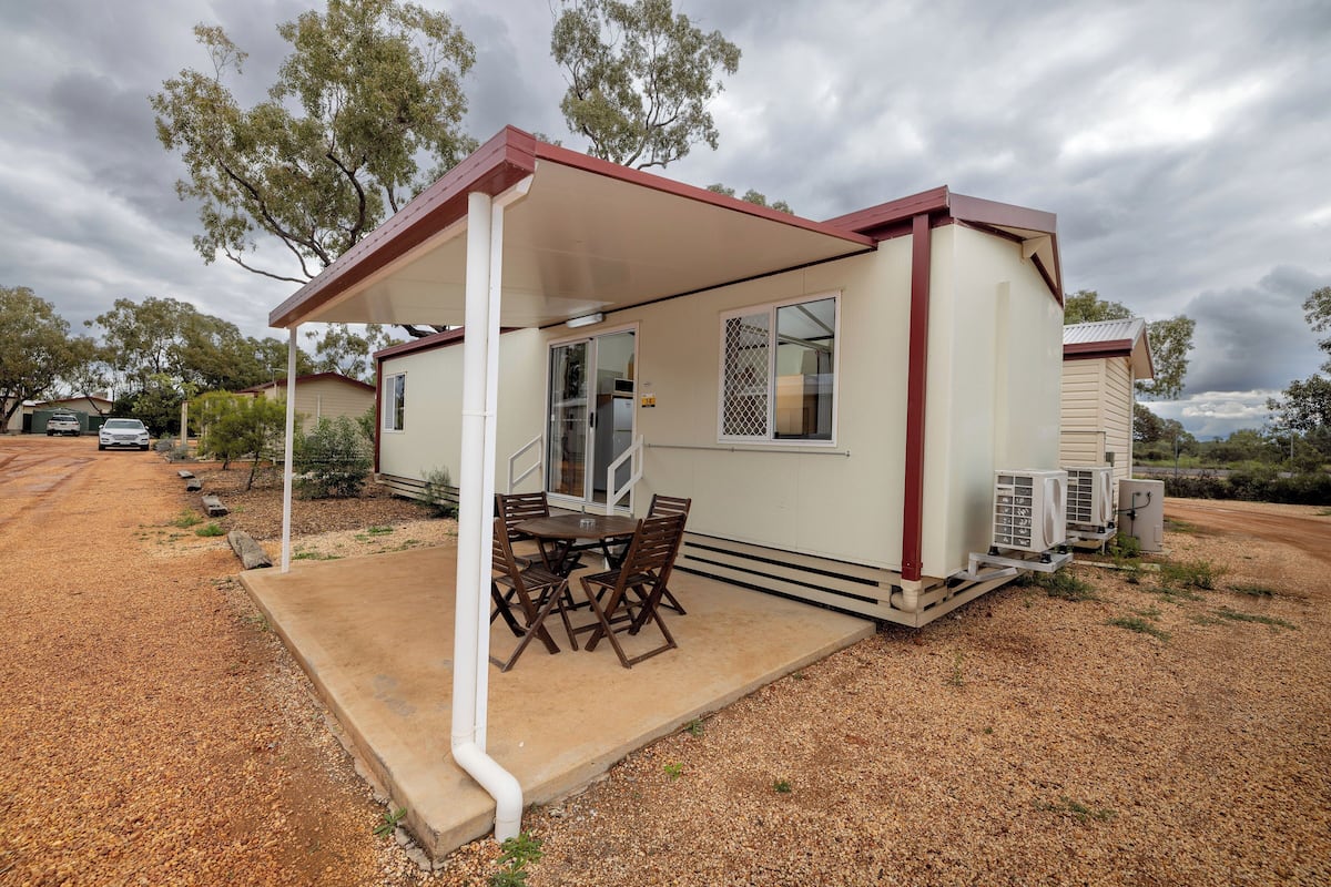 A single-story house with a covered patio, a table and chairs, and an air conditioning unit.