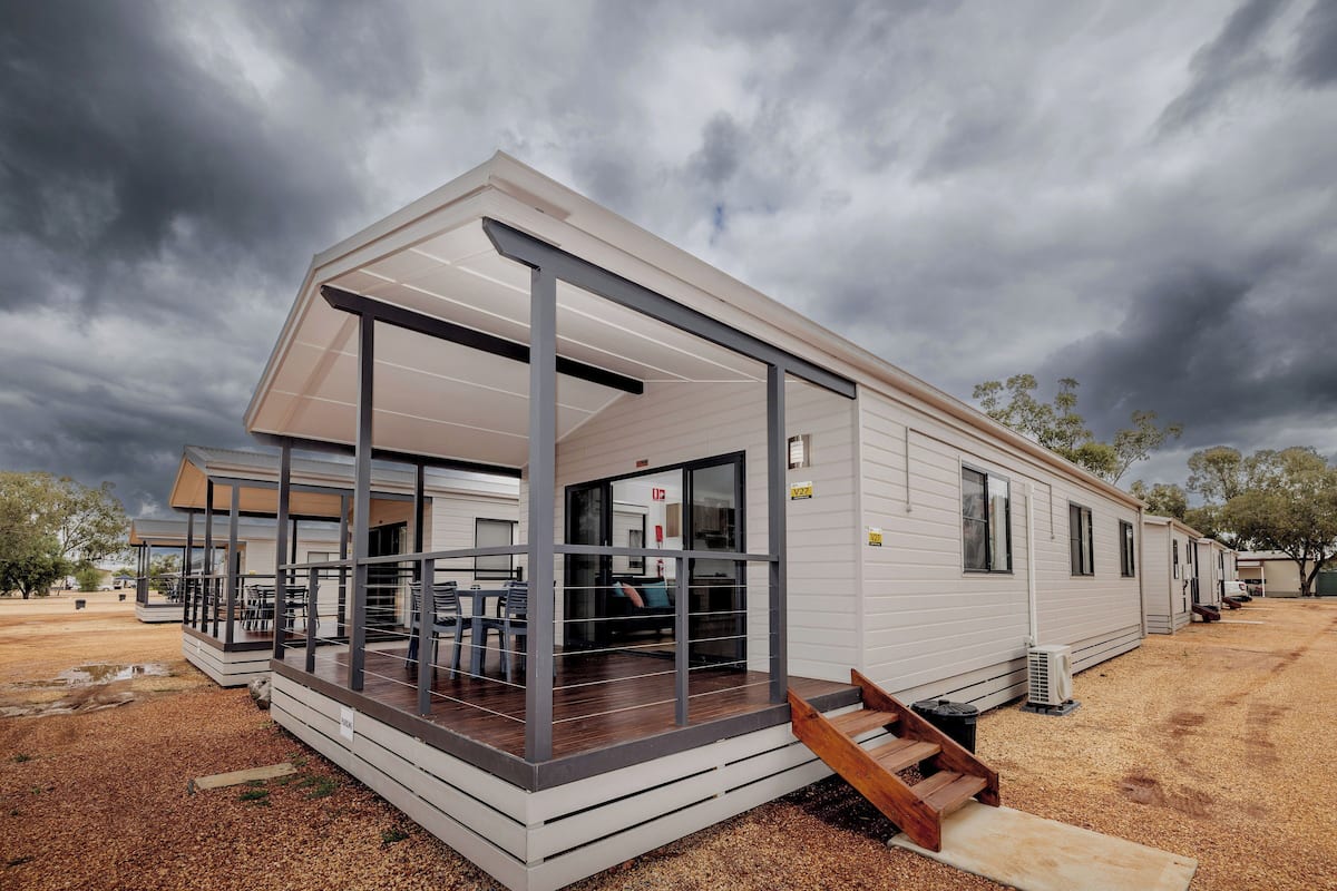 A modern mobile home with a covered porch, outdoor seating, and a gravel driveway.