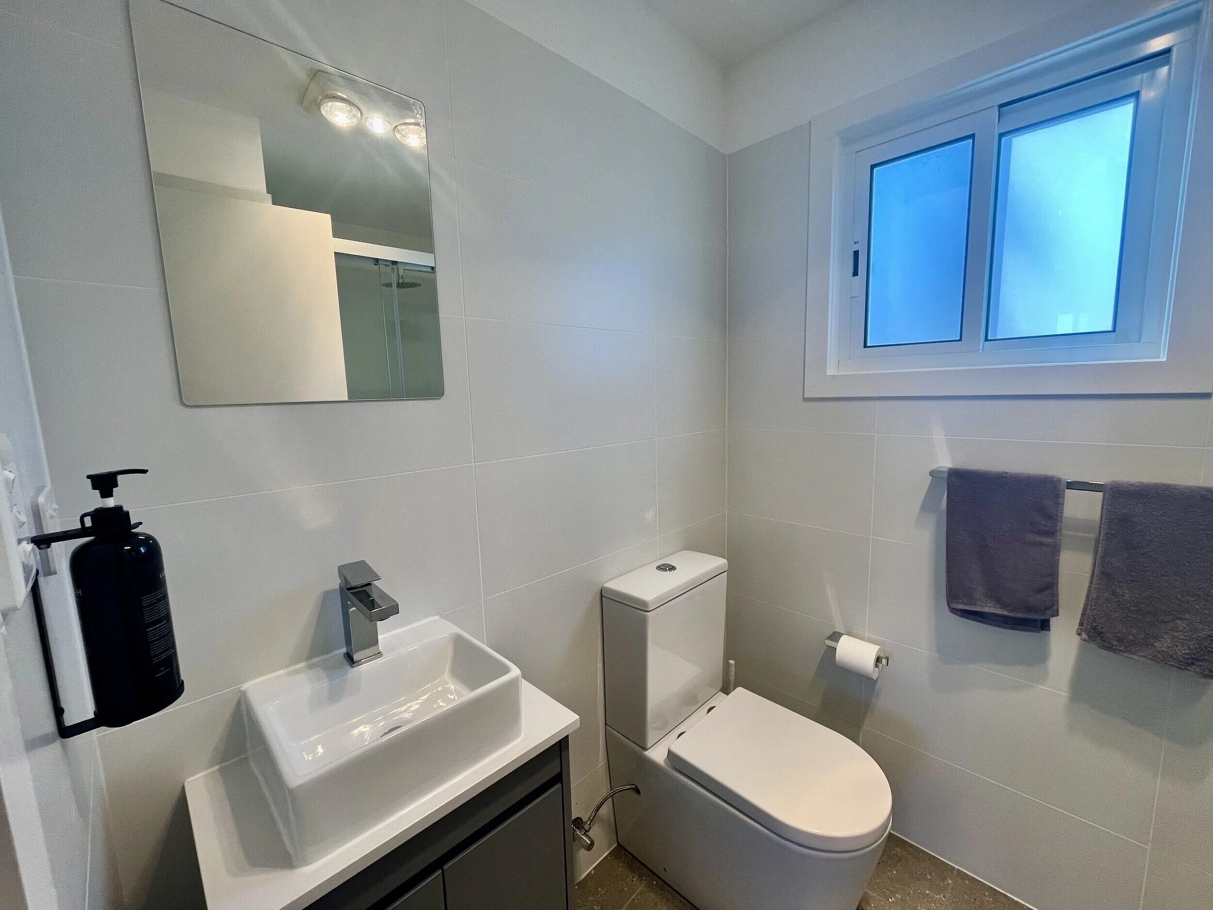 A bathroom with a white sink, a toilet, a mirror, and a window.