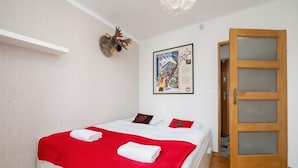 A bedroom with a bed, a red blanket, a white pillow, a framed picture, and a wooden door.
