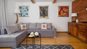 A modern living room with a grey sectional sofa, a small side table with a tray of tea, and three framed artworks on the wall.
