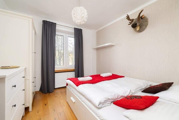 A bedroom with a bed, a dresser, a window with curtains, and a mounted animal head on the wall.