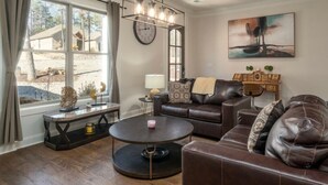 Un salon avec un canapé en cuir, une table basse ronde, une horloge au mur et un tableau accroché au-dessus du canapé.