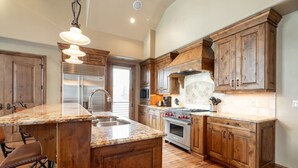 Eine Küche mit Holzschränken, einer Granit-Arbeitsplatte, einem Edelstahlkühlschrank und einem eingebauten Backofen.