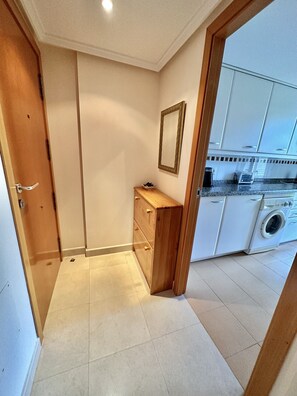 Una cocina compacta con lavadora, un pequeño armario de madera y un espejo en la pared.