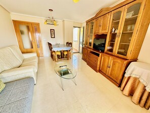A living room with a sofa, a glass coffee table, a dining table with chairs, and a wooden cabinet with glass doors.