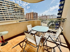 Un balcon avec une table et des chaises, une vue sur les bâtiments environnants et un ciel dégagé.