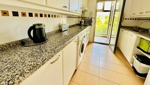A kitchen with a granite countertop, a coffee maker, a washing machine, and a view of the outdoors through a glass door. - A1039 - Quality flat with garage and swimming pool (Villajoyosa)