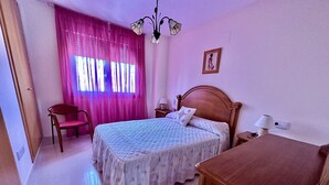 A bedroom with a bed, a chair, a desk, a nightstand, a lamp, and a window with curtains. - A1039 - Quality flat with garage and swimming pool (Villajoyosa)