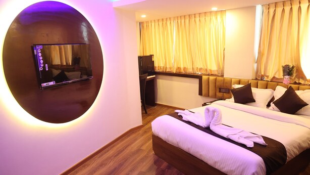 A hotel room with a large bed, a TV mounted on a circular wall, a desk with a computer, and curtains on the windows. - Hotel Air Stay Inn (Mumbai)