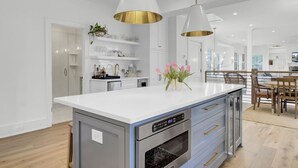 Une cuisine moderne dotée d’un îlot central, d’appareils électroménagers en acier inoxydable et de luminaires suspendus.