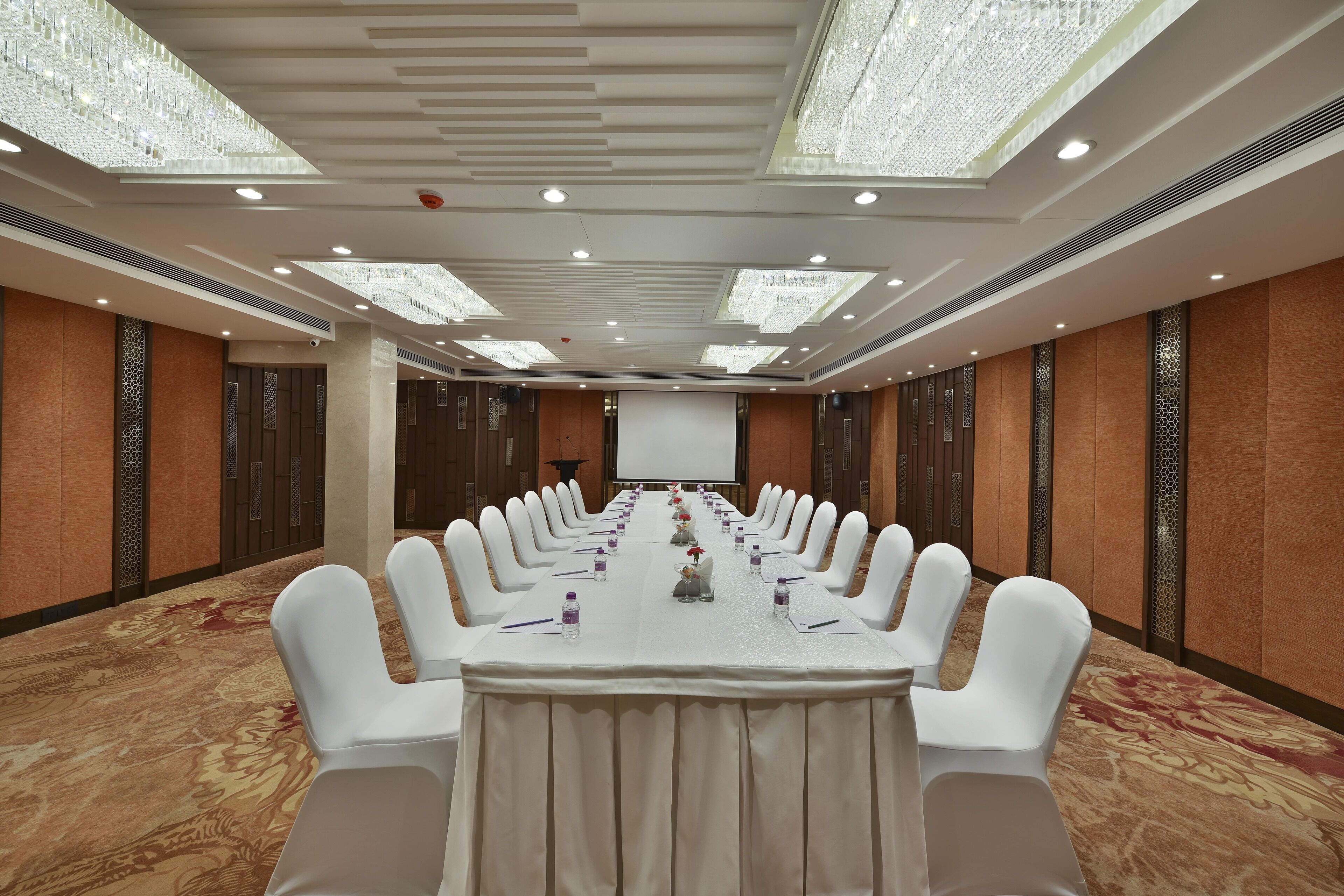 A conference room with a long table, white chairs, and a projector screen.