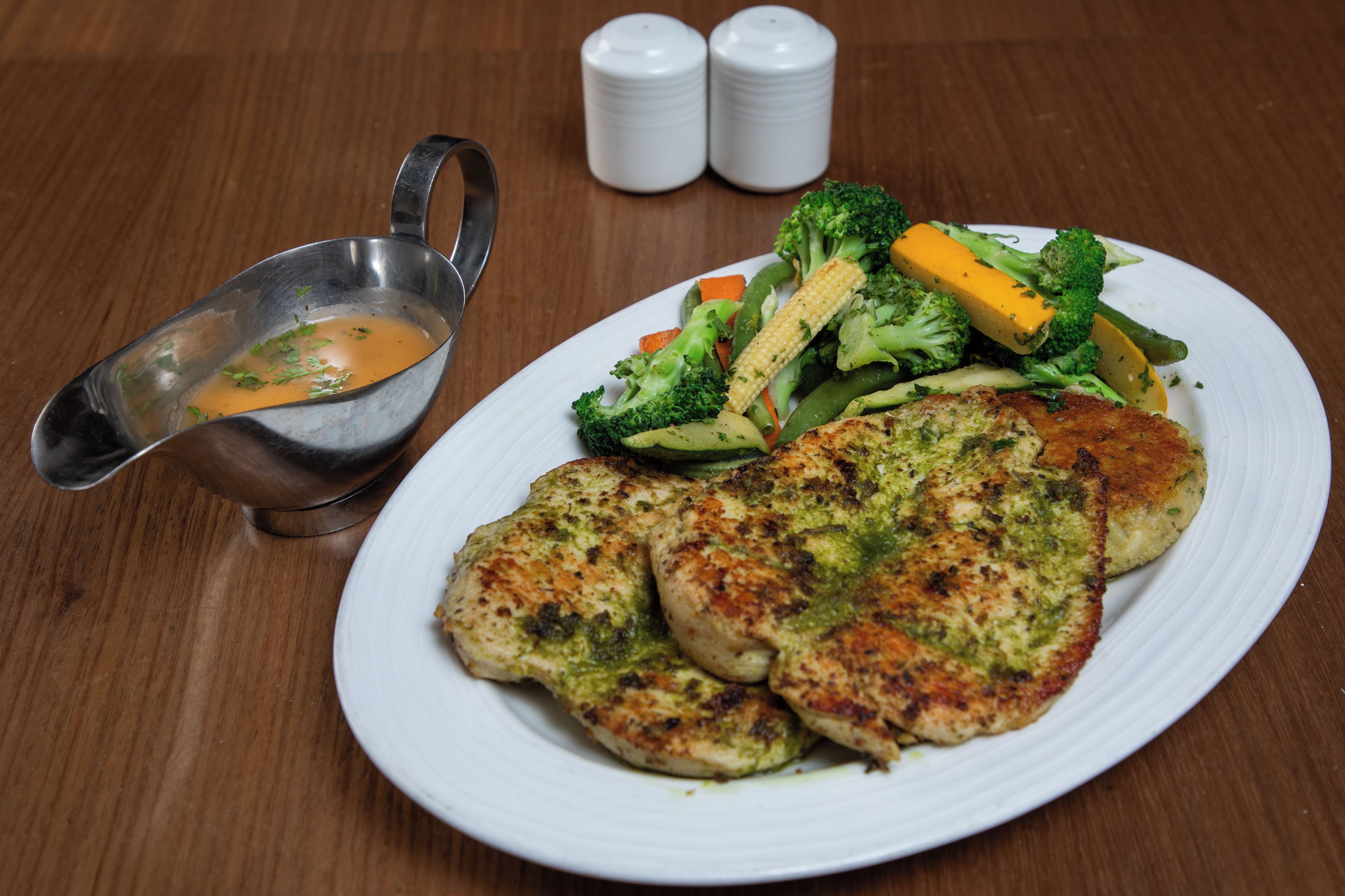A plate of food with a side of gravy and two salt and pepper shakers on a wooden table.
