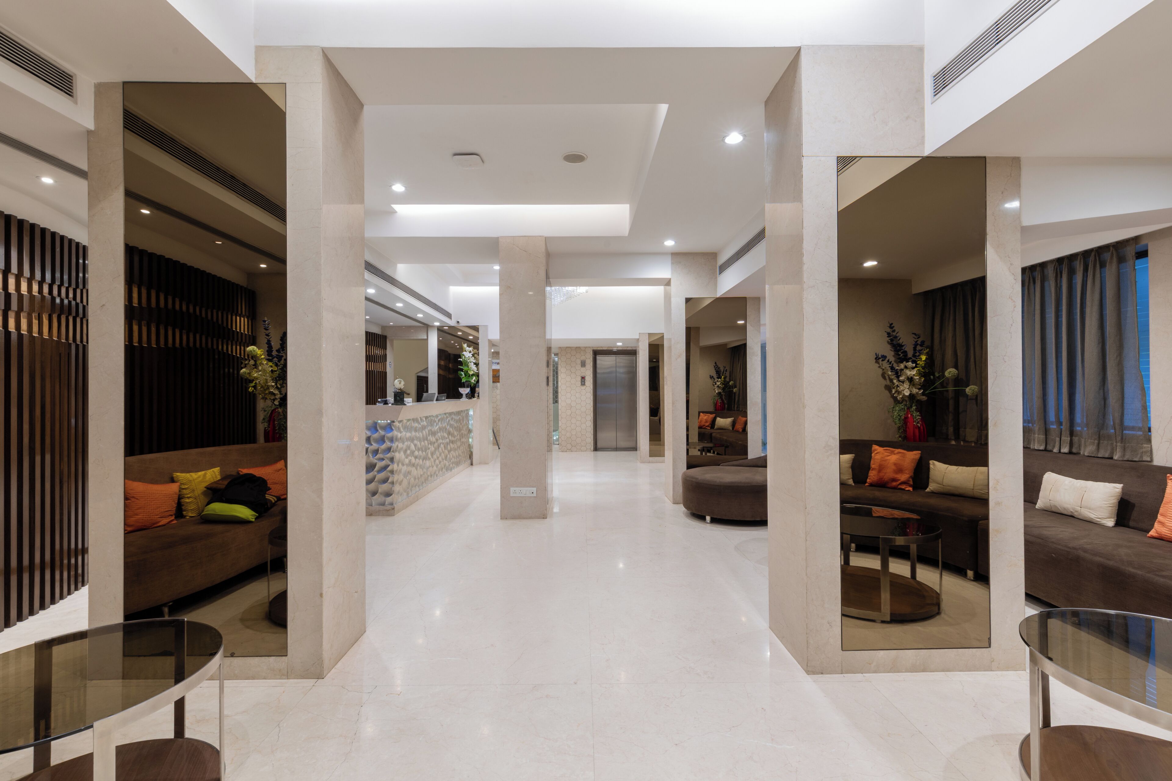 A modern hotel lobby with a central reception desk, seating areas, and a glass coffee table.
