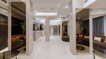 A modern hotel lobby with a central reception desk, seating areas, and a glass coffee table.
