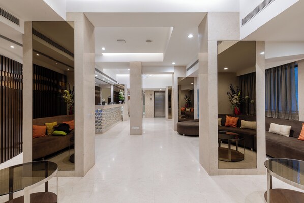 A modern hotel lobby with a central reception desk, seating areas, and a glass coffee table.