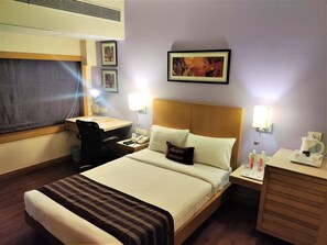 A hotel room with a bed, desk, chair, bedside tables, and a wall-mounted picture.