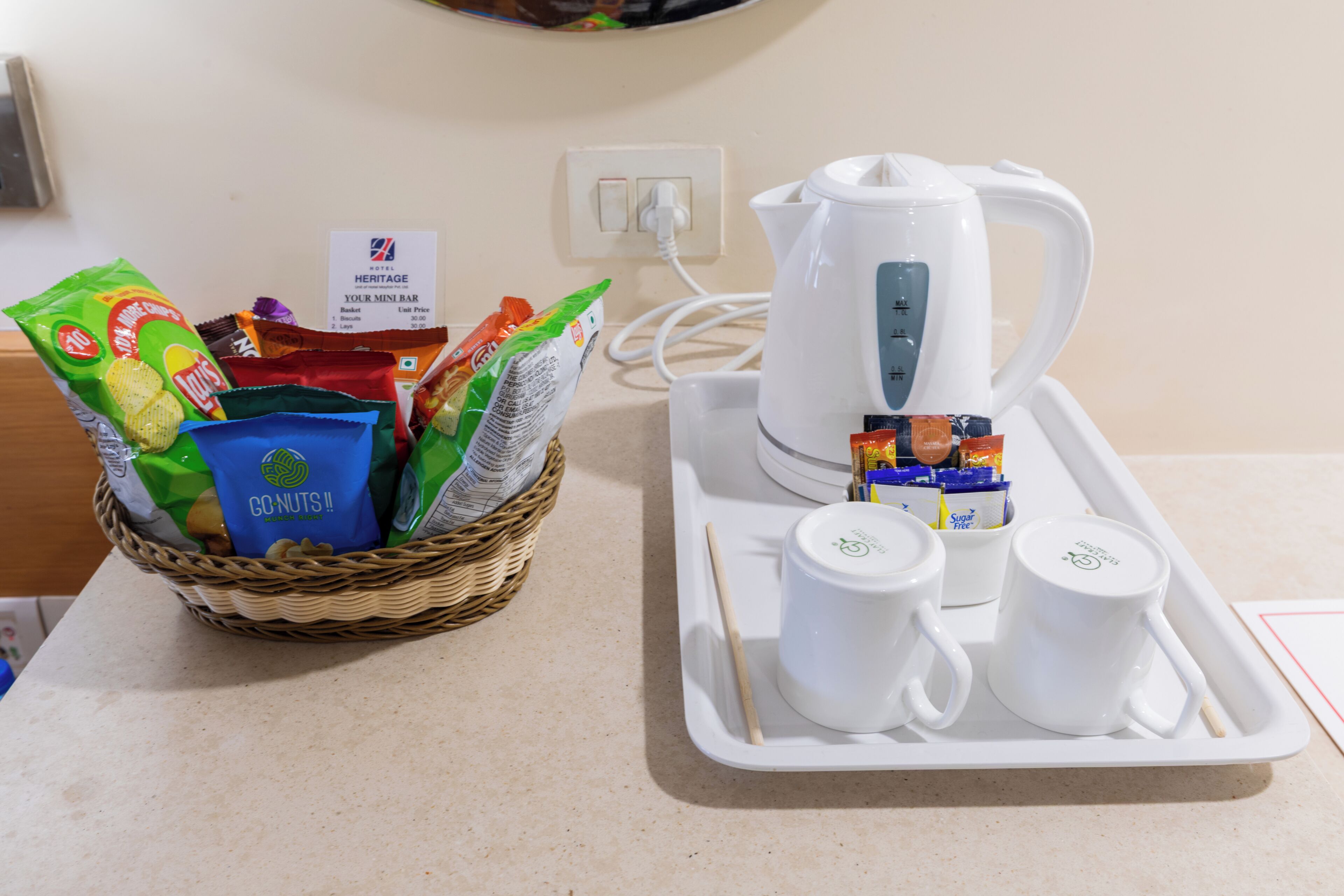 A tray with a kettle, two cups, and a basket of snacks.